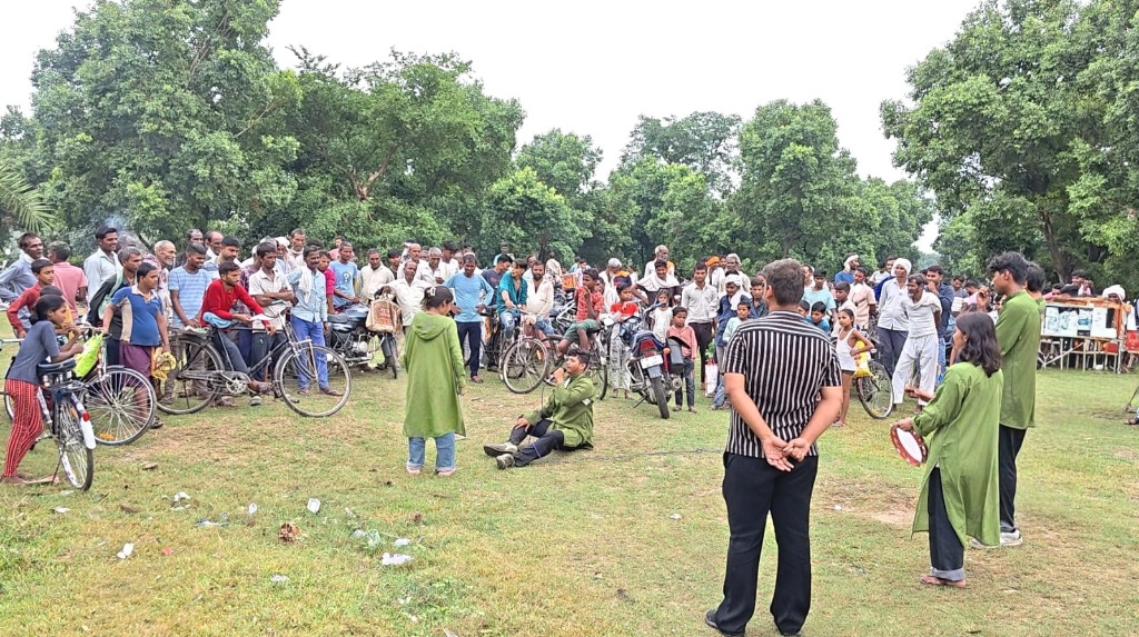 Street play performance in a rural field setting with crowd and bicycles
